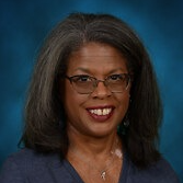 A person with shoulder-length hair, glasses, and a confident smile is pictured against a blue background.